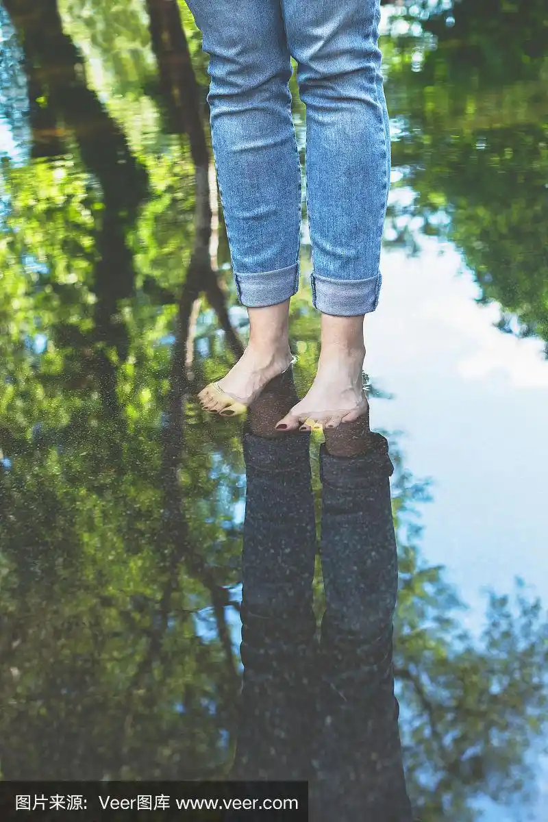 赤脚女人穿着蓝色牛仔裤站在水坑在城市设置