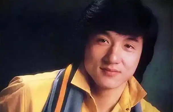 照片中的成龙大哥身穿白色t恤和黑色运动裤,背着一件衣服.