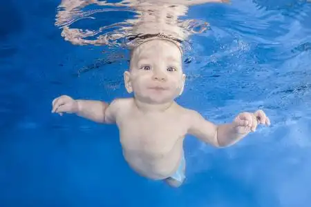 婴儿在蓝色的水背景下在游泳池里游泳.