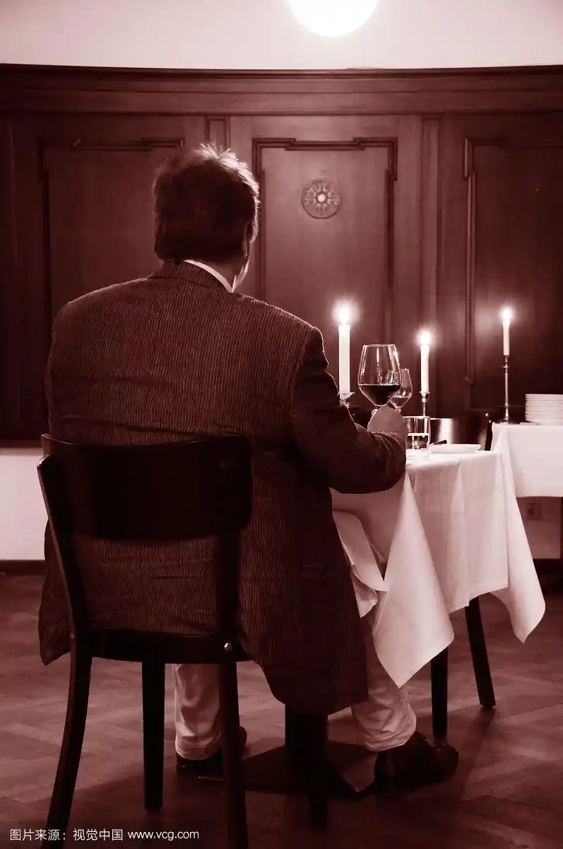 男人坐在桌子上,点着蜡烛,拿着红酒杯喝酒