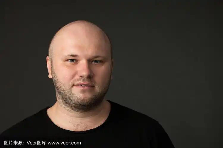 一名35岁剃着光头的大胡子男子的工作室肖像,他穿着黑色t恤,背景是