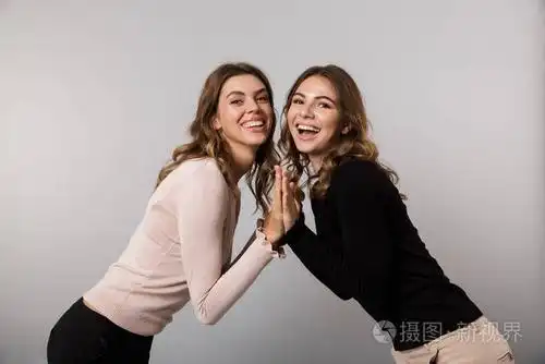 在灰色背景下,两个快乐的女人一起笑和摆姿势照片-正版商用图片14tvcx