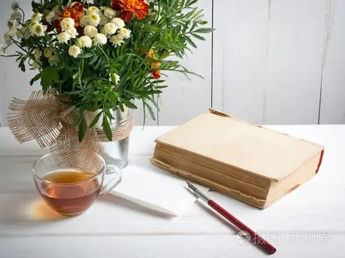 万寿菊鲜花花束用老书和杯茶和笔尖笔上
