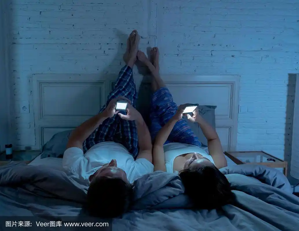 微笑迷人的年轻男女夫妇一起躺在床上使用智能手机.