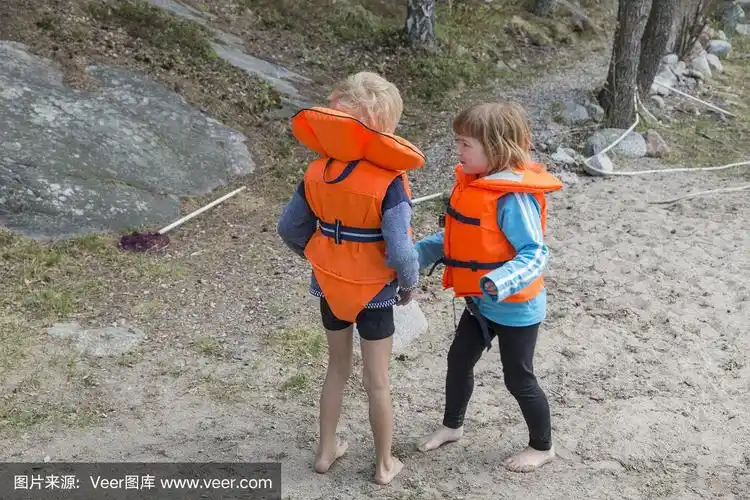 光着脚的小男孩和小女孩穿着亮橙色的救生衣