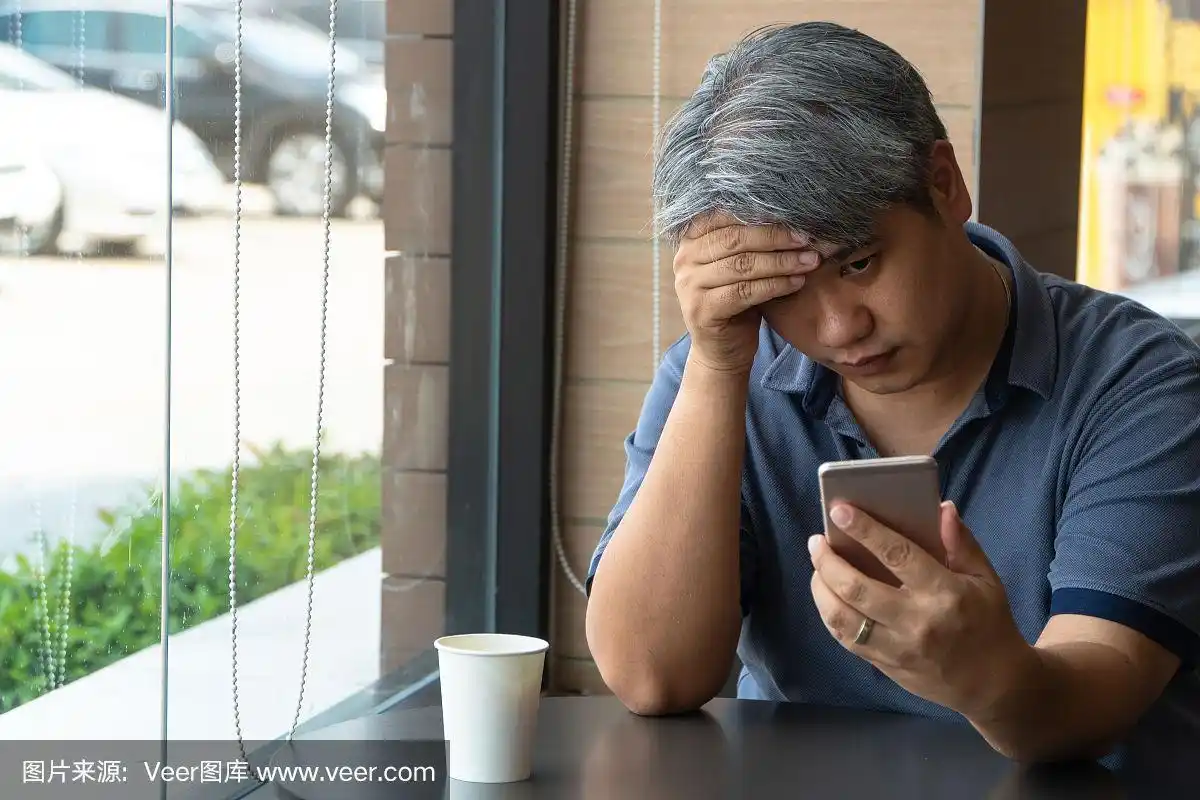 中年亚洲男人(40岁),压力和疲倦,使用智能手机,坐在快餐店.