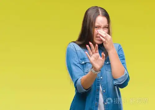 年轻的白种人美丽的女人在孤立的背景上闻到了一些臭味和令人恶心的