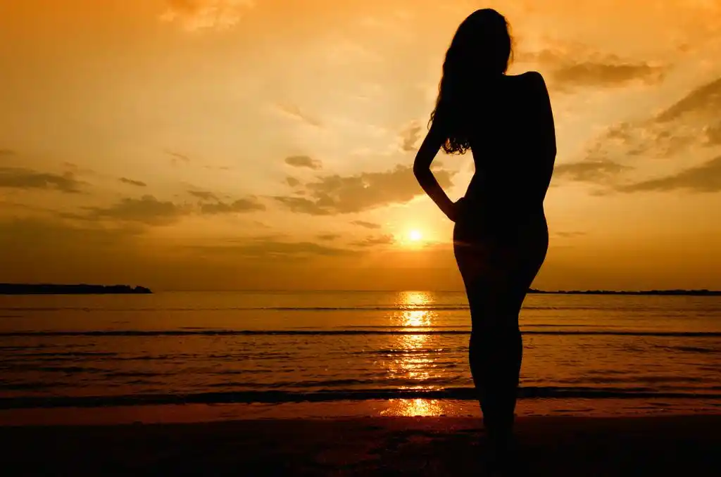 日出时在海滩上的性感女人的剪影