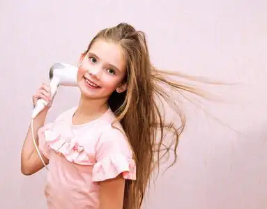 可爱的微笑着的小女孩用吹风机把她的长发擦干照片