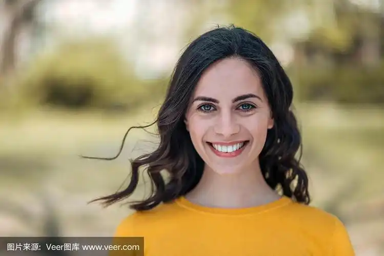 一个年轻的黑发女人的大头照,露齿微笑在一个明亮的户外背景.