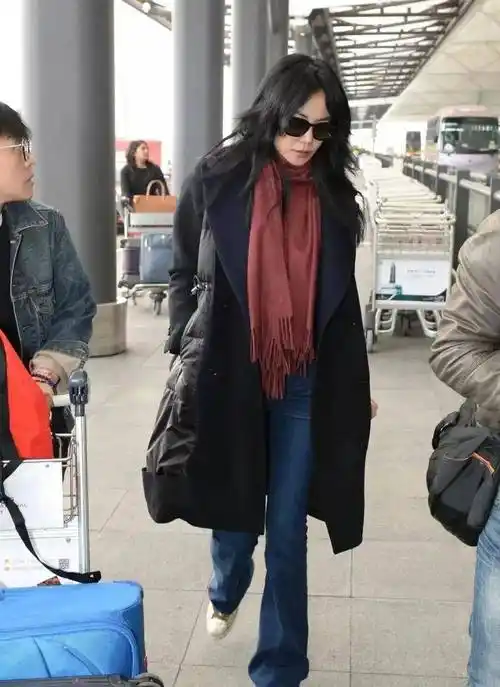 在机场,王菲选择了一件拼接羽绒服搭配微喇叭牛仔裤和酒红色围巾.