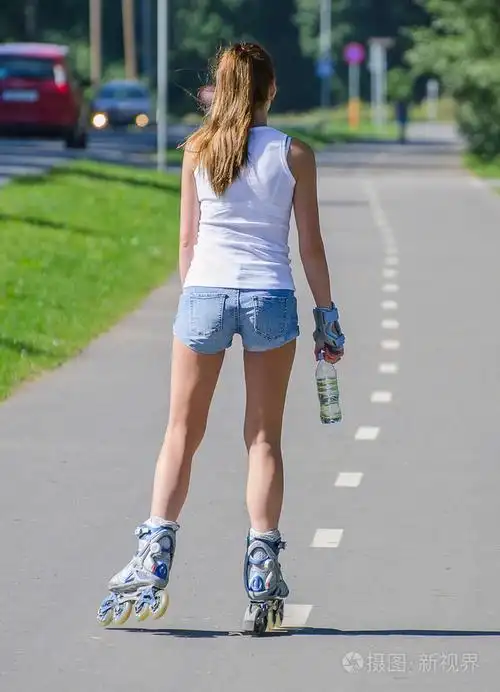 带瓶水的女人骑在公园里的溜冰鞋后视图