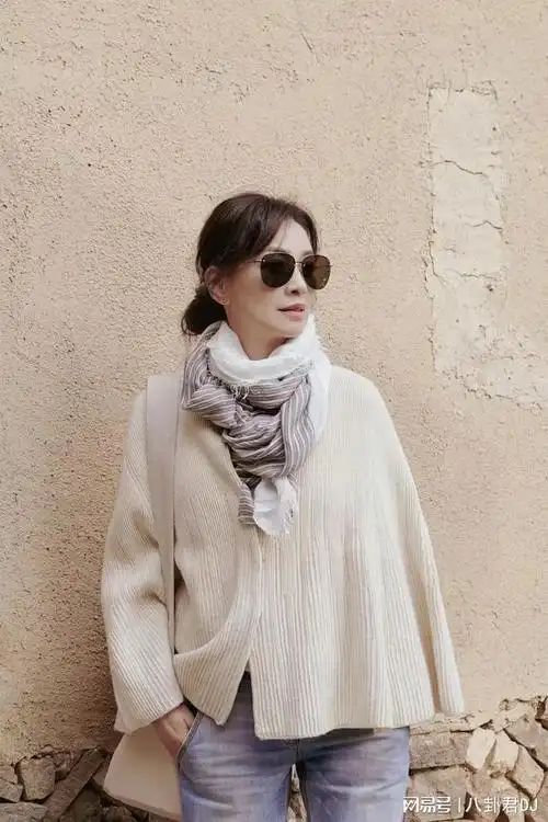 "视频中的张庭穿着米白色针织开衫,搭配浅色牛仔裤,坐在小店门口的