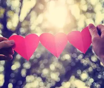 双手捧着一串纸心,在阳光下向太阳升起