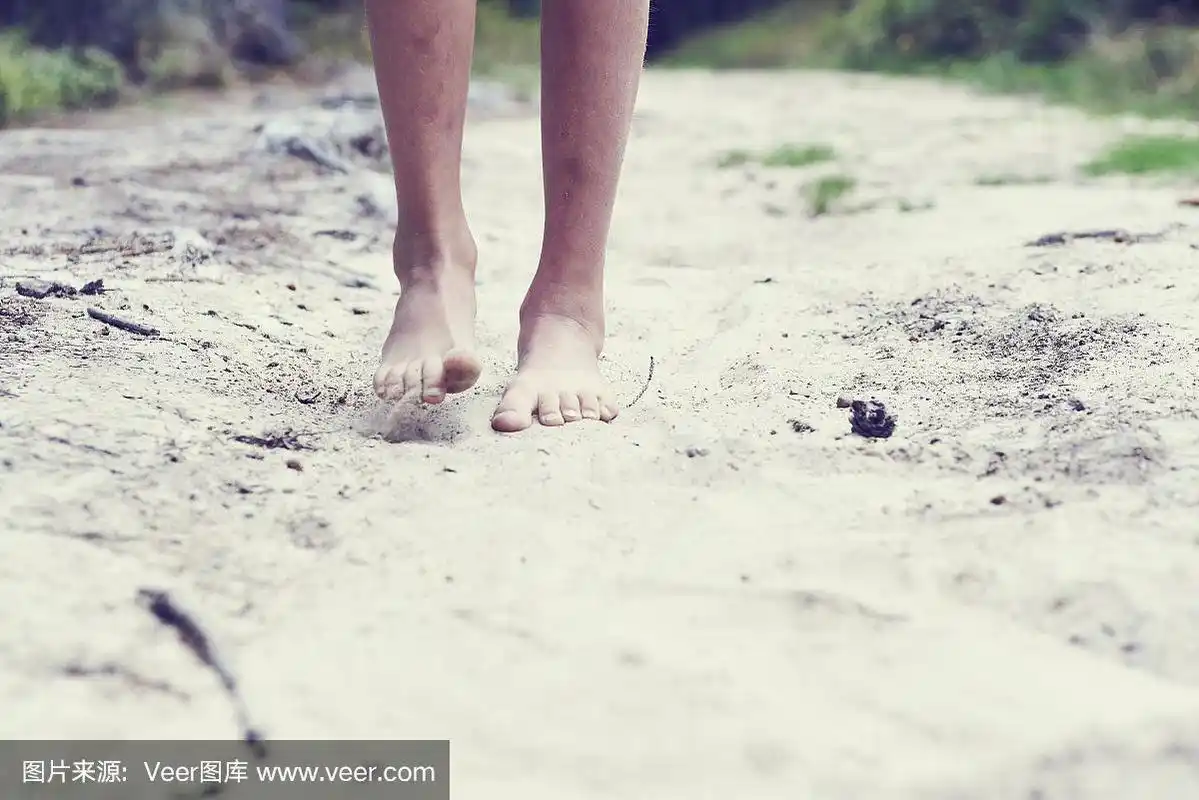小女孩赤着脚走在森林的沙路上.