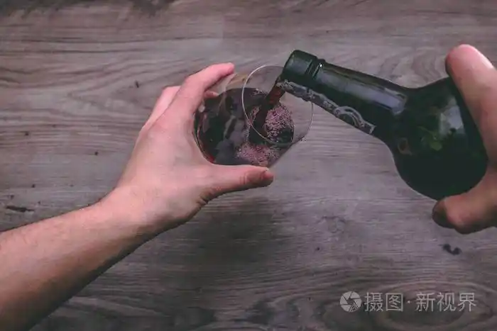 从一只手的顶部拿着一个红酒瓶并倒入玻璃