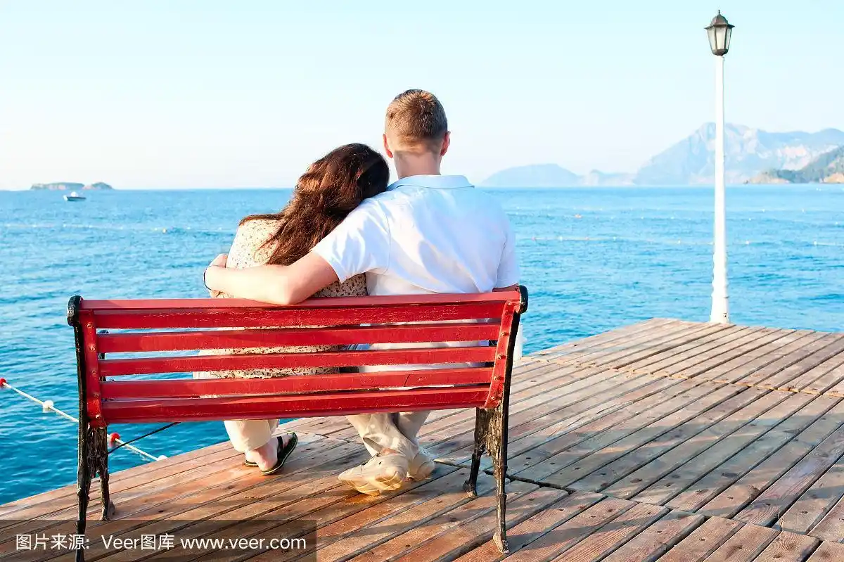 一对情侣坐在海边的长椅上相拥