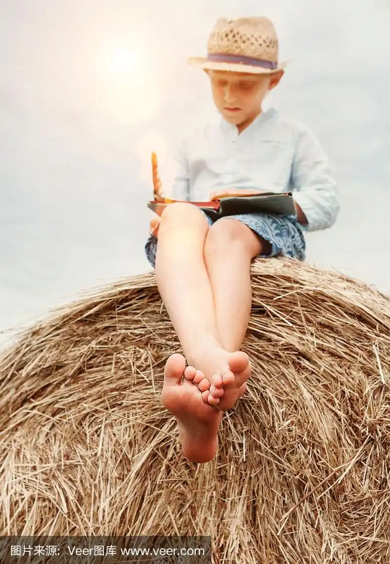 光着脚的男孩坐在草堆上看书