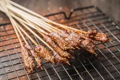 黑色烤架上放着几串撒着辣椒面的油炸牛肉小串