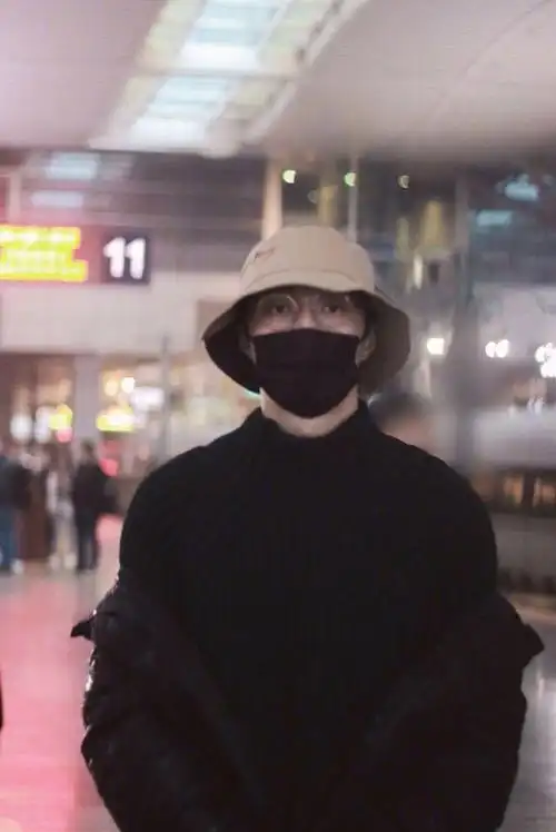 张艺兴行程饭拍图,身着深色毛衣配亮闪羽绒服,渔夫帽搭配边框眼镜