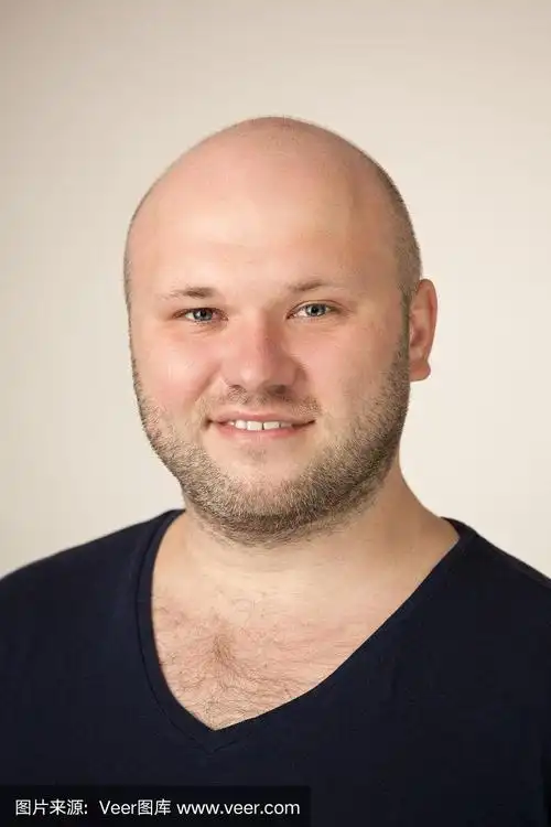 一名35岁剃着光头的大胡子男子的工作室肖像,他穿着一件蓝色t恤,米色