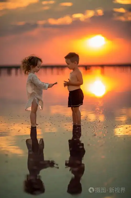 日落时两个小孩子在海滩上玩耍孩子们在水里玩水的反射