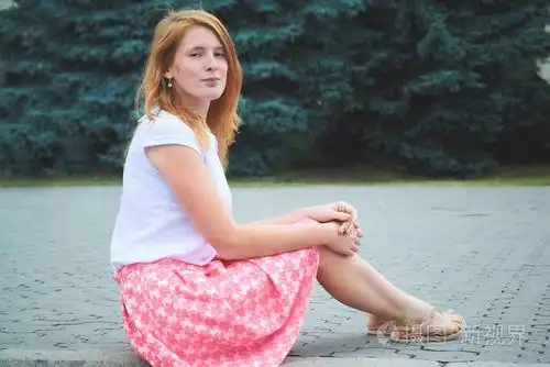 女孩穿着白色上衣和粉红色的裙子坐在城市的地面上