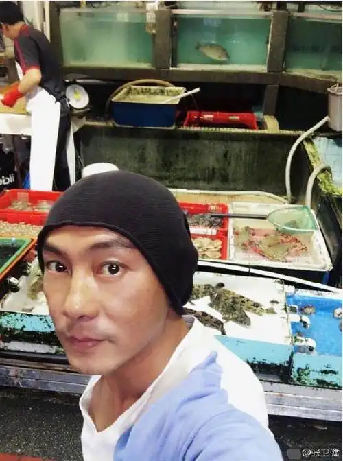 来看下这张自拍,张卫健戴着针织帽在一个鱼档面前自拍,这个就是他光顾