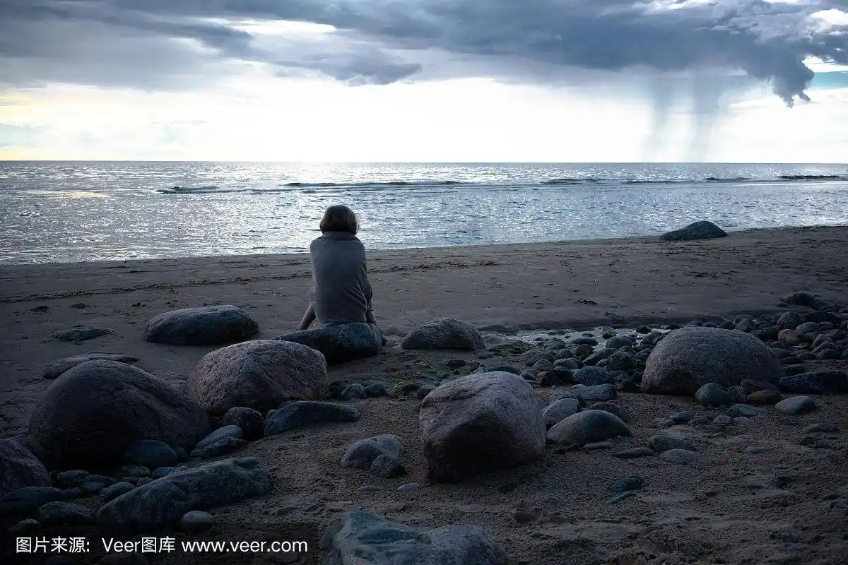 悲伤的女孩坐在海滩的岩石上