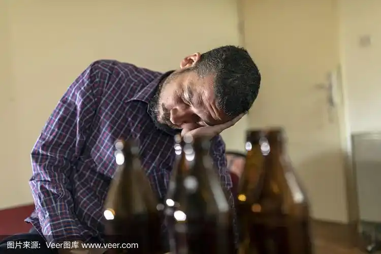 年轻悲伤的醉酒男子喝啤酒和酒精感到浪费,孤独和绝望