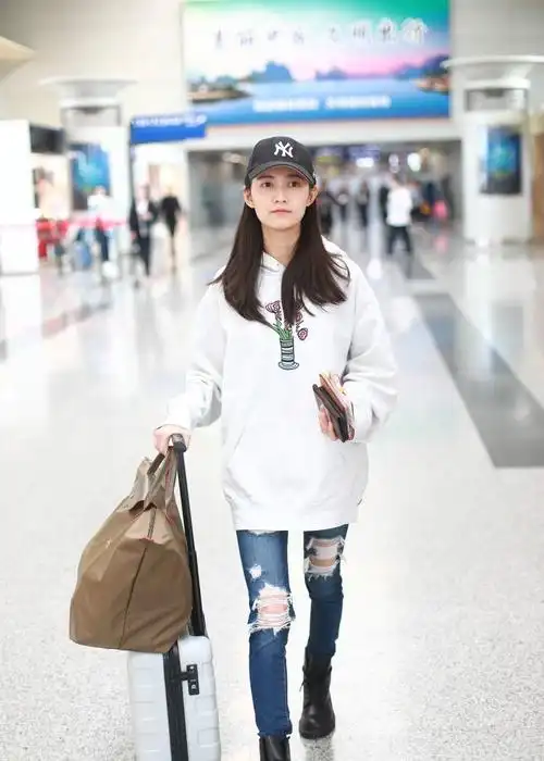 陈钰琪穿白色卫衣搭配破洞牛仔裤现身机场,戴黑色棒球帽皮肤白皙