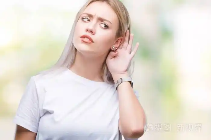 年轻的金发女人在孤立的背景上微笑,用手捂住耳朵听谣言或流言蜚语.