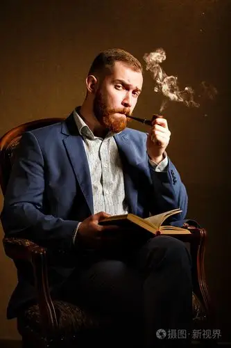 英俊的年轻男子吸烟管和读的书的蓝色西装的肖像