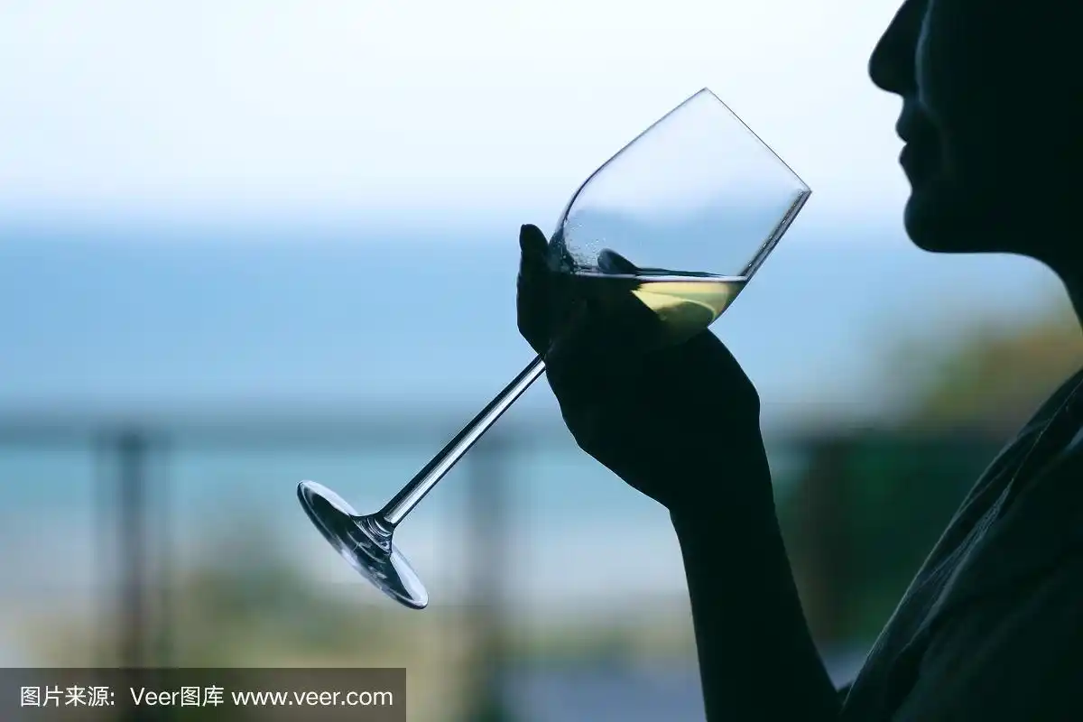 一个女人拿着酒杯喝着模糊的大海背景