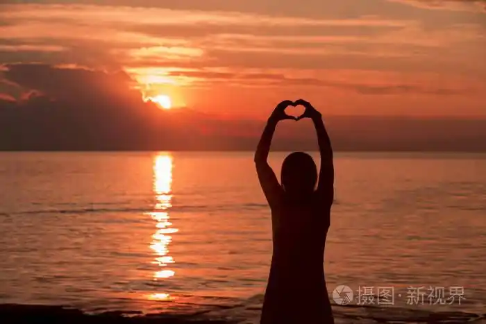 女性手的心形轮廓与红色魔术日落