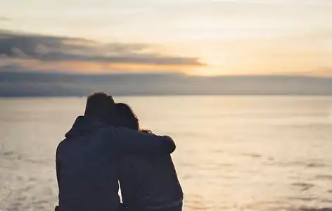 一起看日出夫妇在背景海洋日出在沙滩上拥抱,两个浪漫的人的侧影拥抱