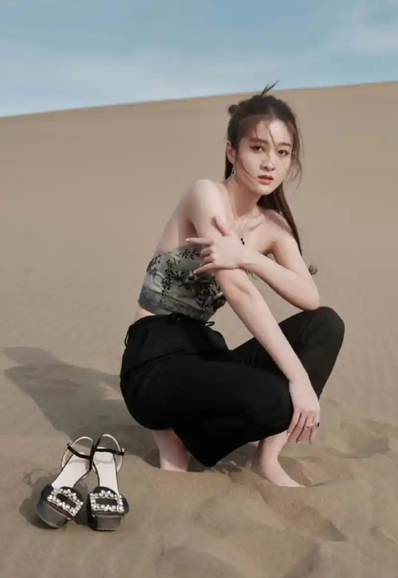张雪迎在沙漠里参加活动,高跟鞋站不稳,用手提着拍照,回身看镜头甜笑