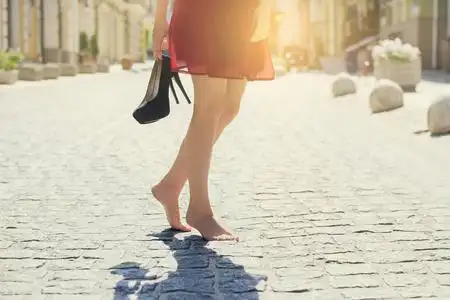 穿着红色高雅连衣裙的妇女, 手捧高跟鞋, 赤脚走在城里.关闭裁剪照片.