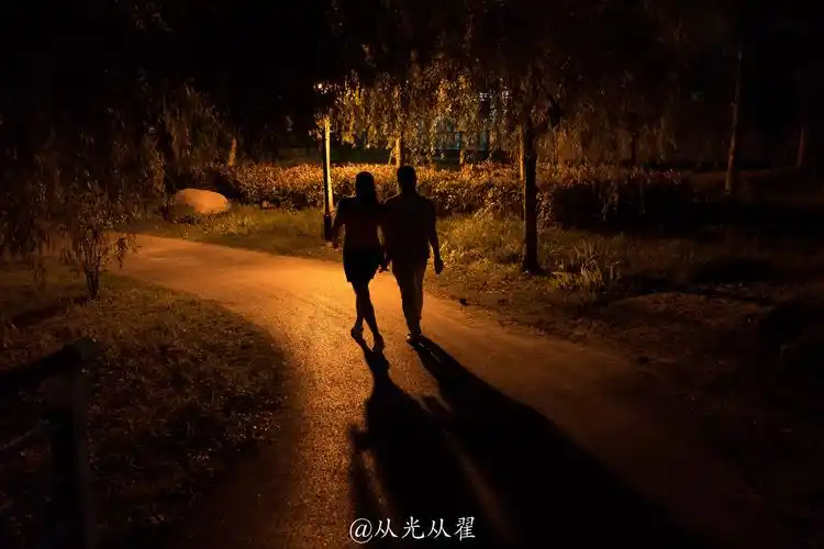 夜晚,一对在公园里散步的情侣从光从翟关注