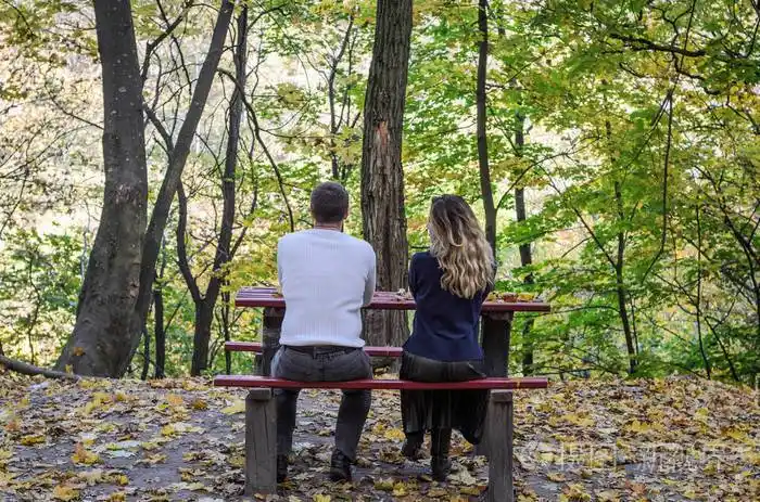 相爱的情侣坐在秋天公园的长凳上的黄落叶之间