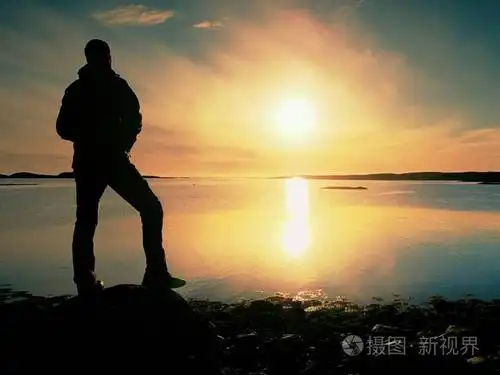 美丽的夏日日落在海边.站立的人与背包在海洋反对日落