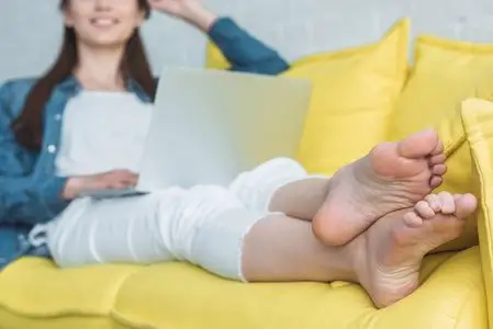 赤脚微笑在家沙发上使用笔记本电脑的微笑赤脚女孩裁剪镜头照片