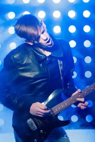 年轻的摇滚音乐家弹电吉他和唱歌.对背景的聚光灯的摇滚明星