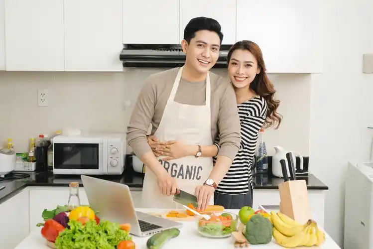 幸福的夫妇准备健康新鲜的蔬菜沙拉在厨房里