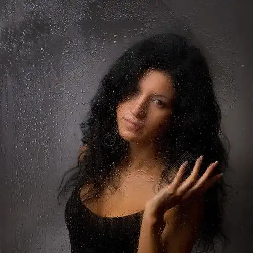 美丽的女孩,在暗背景上淋湿的玻璃后面.