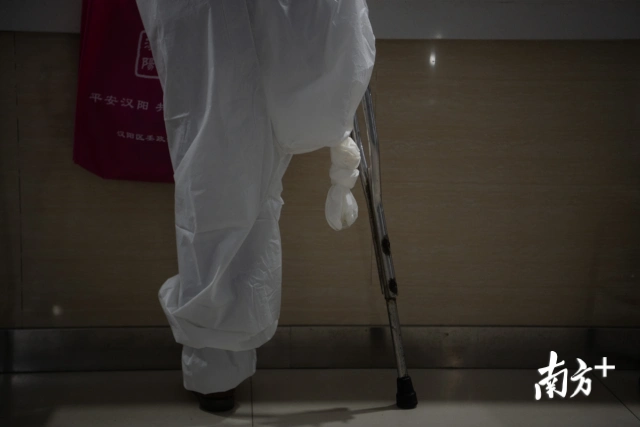 一身白色连体隔离衣,右腿裤管半空中打了一个结,拄着一副拐杖,58岁的