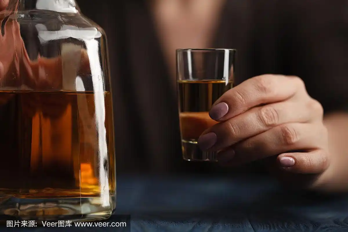 在深色背景下喝酒的女人.专注于酒杯