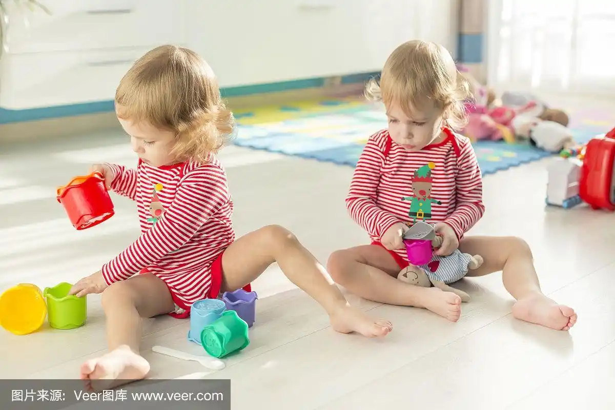 在阳光明媚的公寓里,可爱的双胞胎光着脚坐在地板上