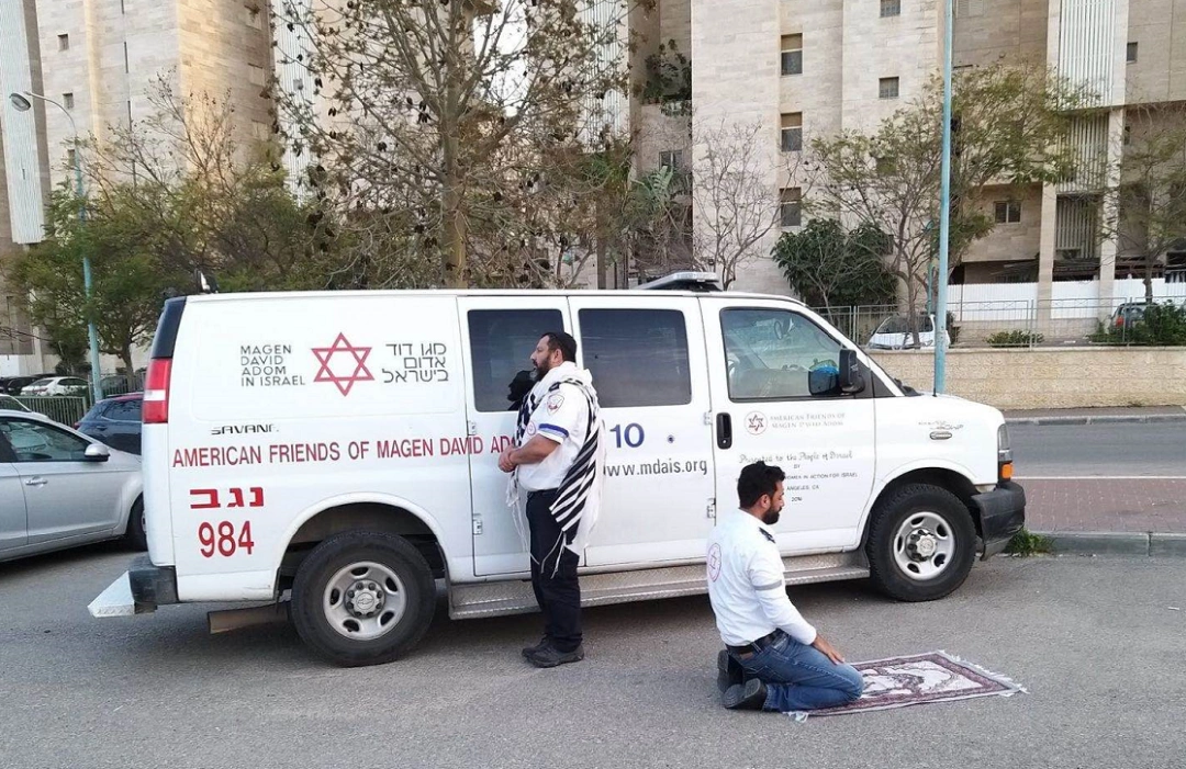 以色列的两名医护人员利用短暂的休息时间在救护车前背对背祈祷,他们