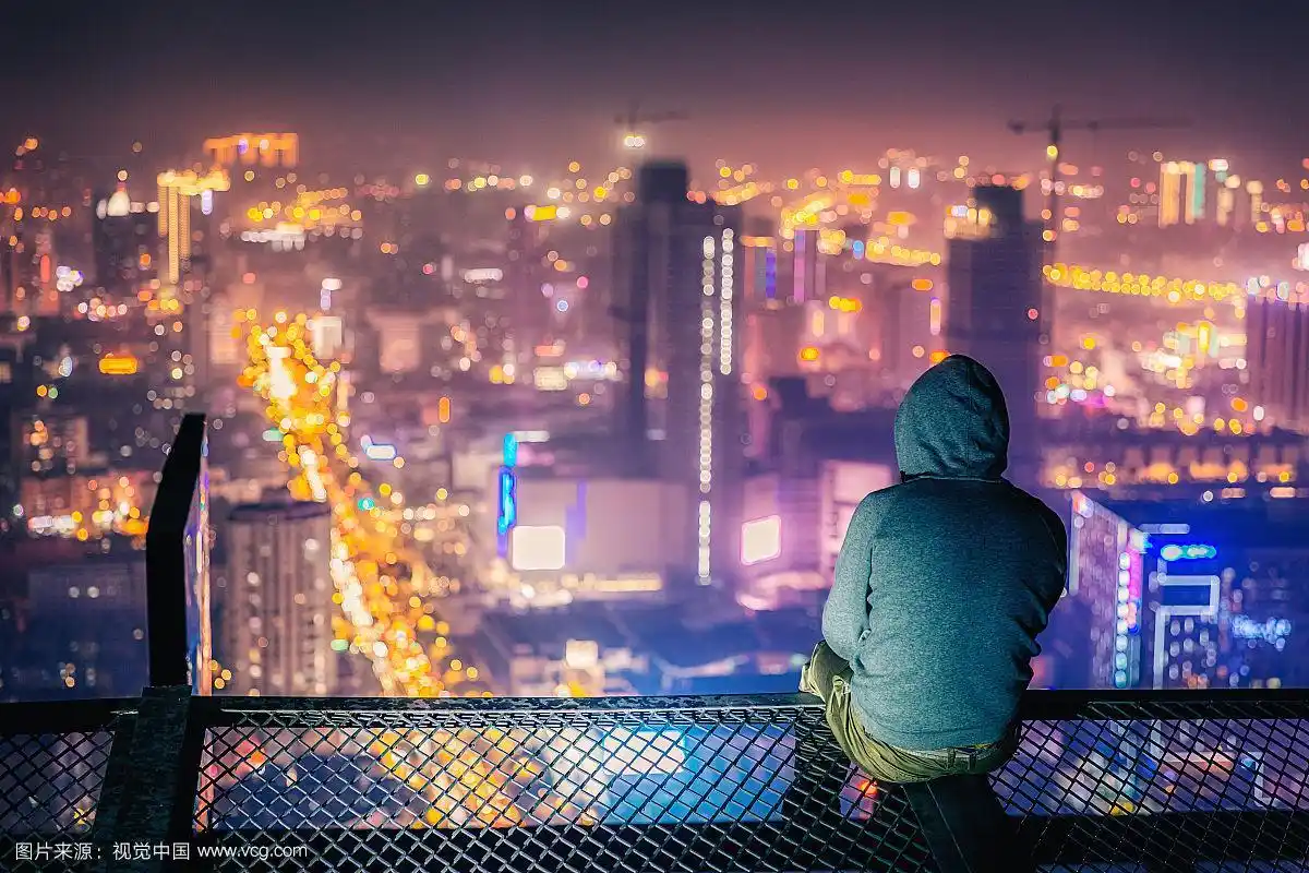 繁华城市楼顶上俯瞰城市夜景的男人背影